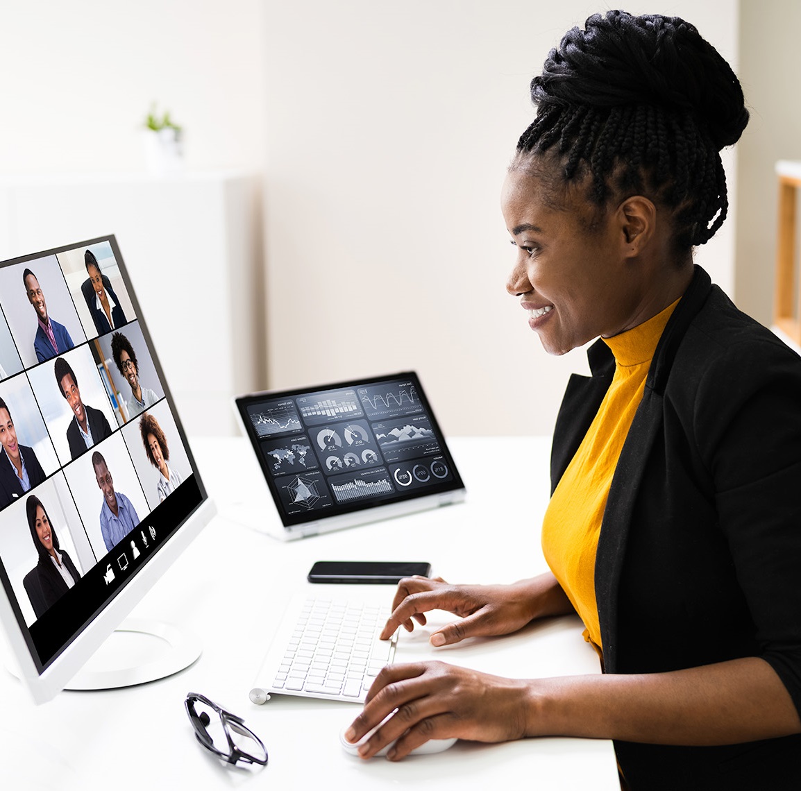 Mulher sentada à mesa em frente a um computador, participando de uma chamada de vídeo enquanto segura o mouse.