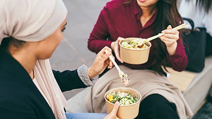 Duas mulheres comem uma salada com talheres descartáveis